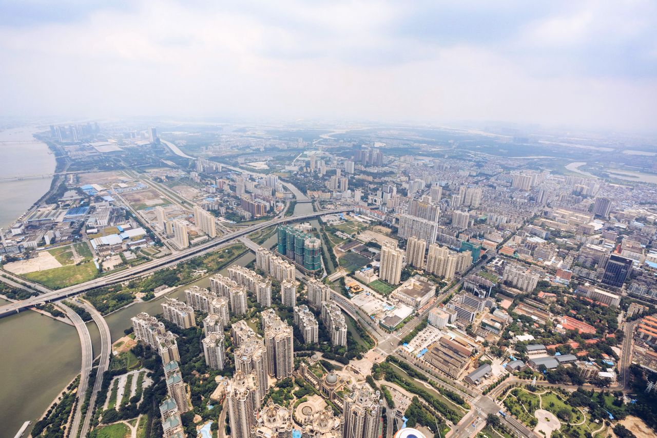 Drone view of modern city district with modern buildings and roads located near river against cloudy sky in summer day